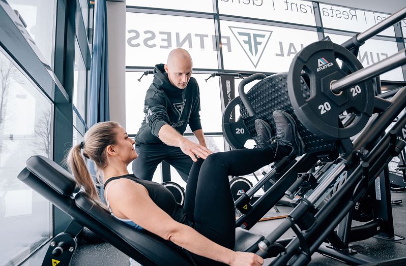 Frau beim Krafttraining an der Beinpresse mit Trainer.