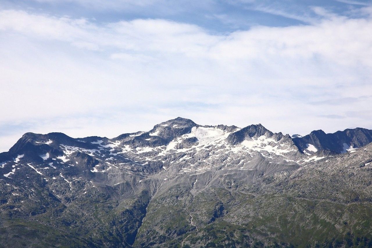 Felsige Bergkette mit schneebedeckten Gipfeln und grünen Hängen unter bewölktem Himmel