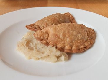 Auf einem Teller sind zwei Fleischkrapfen mit Sauerkraut.