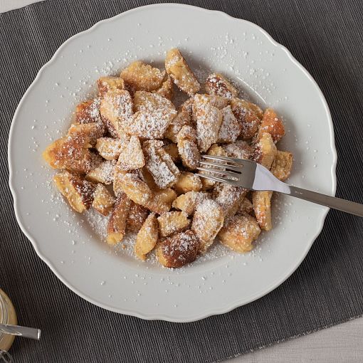 Ein Kaiserschmarrn mit Staubzucker bestreut steht am Tisch.