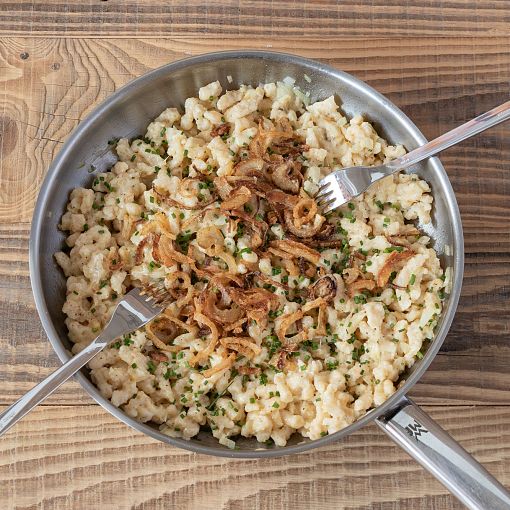 Eine Pfanne mit Kasnocken und Röstzwiebeln mit zwei Gabeln.