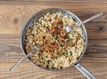 Eine Pfanne mit Kasnocken und Röstzwiebeln mit zwei Gabeln.