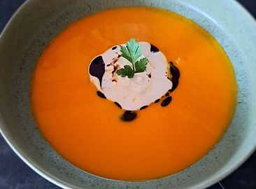 In einem Suppenteller ist die Kürbis-Apfel Cremesuppe angerichtet und mit Schlagobers und Kürbiskernöl garniert.