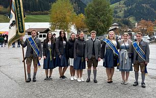 unge Menschen in Tracht vor herbstlichen Bäumen und Bergen im Großarltal, Österreich. Sie tragen traditionelle Kleidung und stehen dicht beieinander.