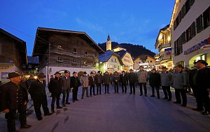 Im Ortszentrum von Großarl stehen die Männer im Kreis für das traditionelle Ölbergsingen und Leiden Christi Singen. Im Hintergrund sieht man die Kirche.