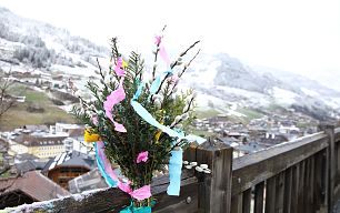 Palmzweige mit bunten Bändern vor schneebedecktem Tal im Großarltal, auf einem Holzzaun befestigt.