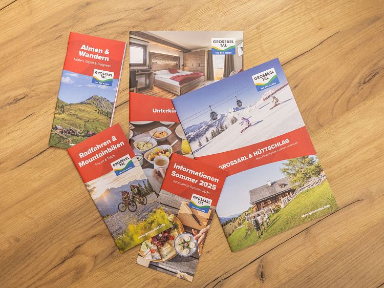 Fünf Prospekte zu Aktivitäten im Großarltal, darunter Wandern, Radfahren und regionale Kulinarik, auf einem Holztisch arrangiert.