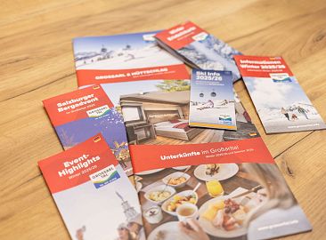 Mehrere bunte Broschüren zu Großarltal-Urlaub auf Holztisch zeigen Aktivitäten und Unterkünfte.