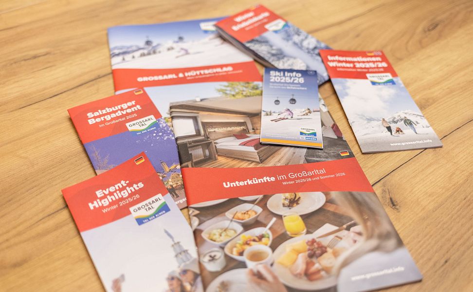 Mehrere bunte Broschüren zu Großarltal-Urlaub auf Holztisch zeigen Aktivitäten und Unterkünfte.