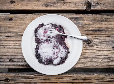 Schwarzbeernocken mit Zucker und Gabel auf weißem Teller auf rustikalem Holztisch.
