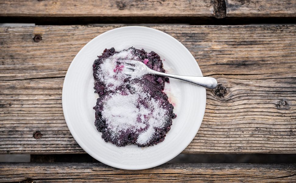Schwarzbeernocken mit Zucker und Gabel auf weißem Teller auf rustikalem Holztisch.